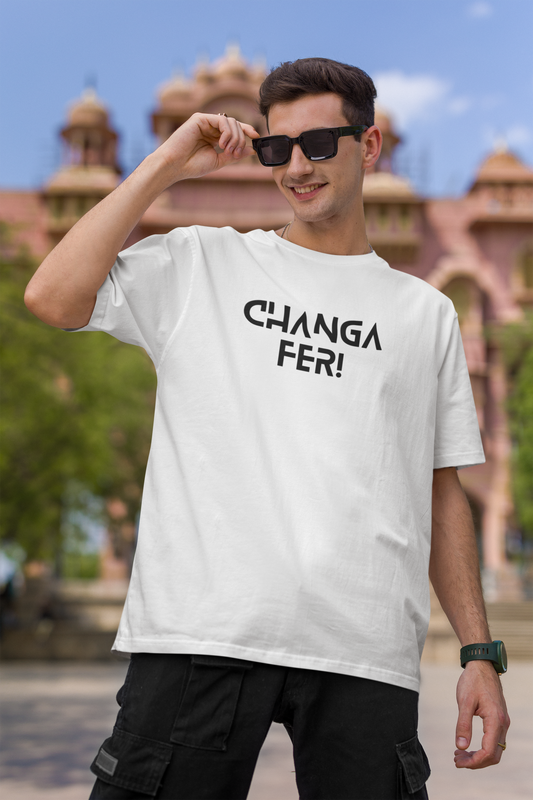 Man wearing a white t-shirt with 'CHANGA FER!' text, posing outdoors with a blurred architectural background.